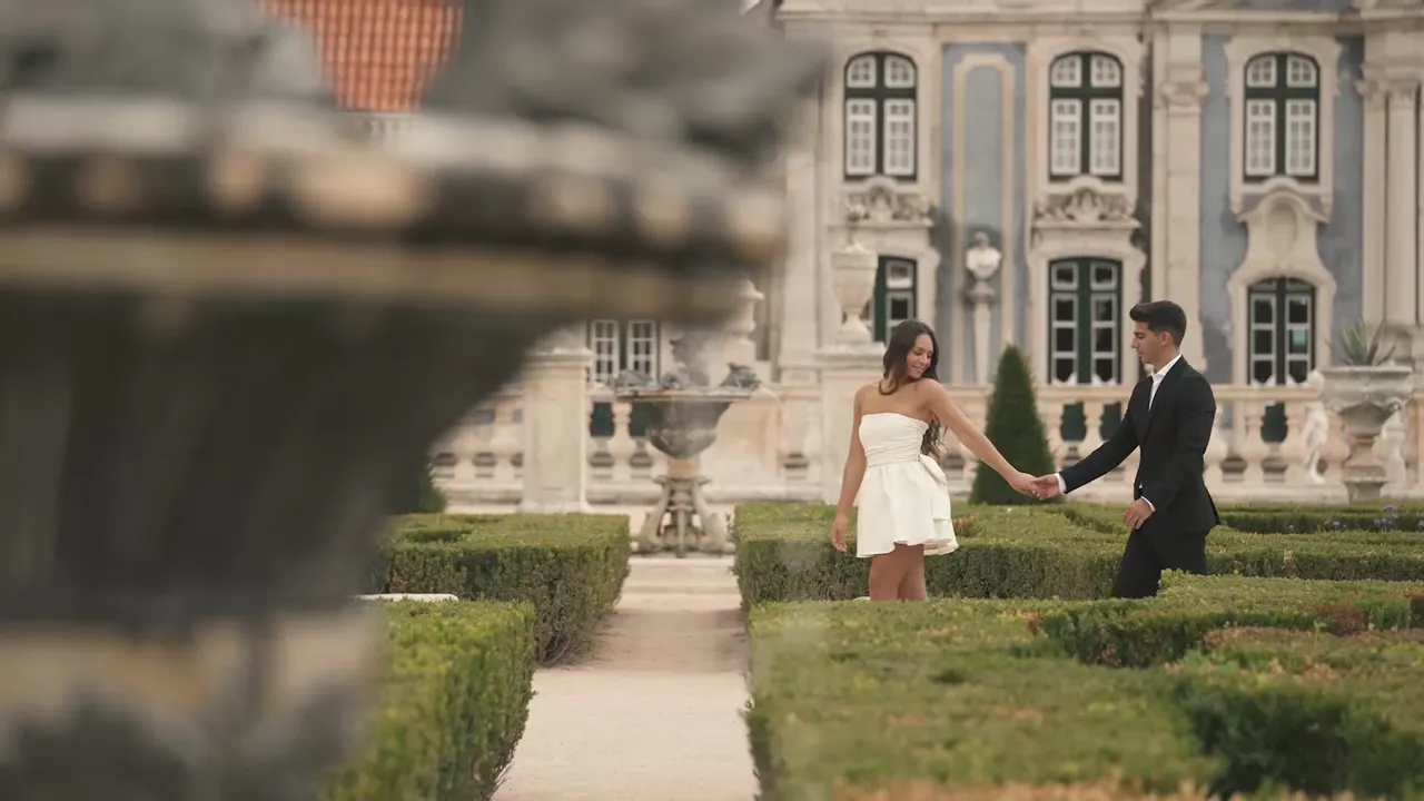 A couple holding hands in the clipped hedge gardens in front of Palácio de Queluz, wedding film by VIP Weddings Films